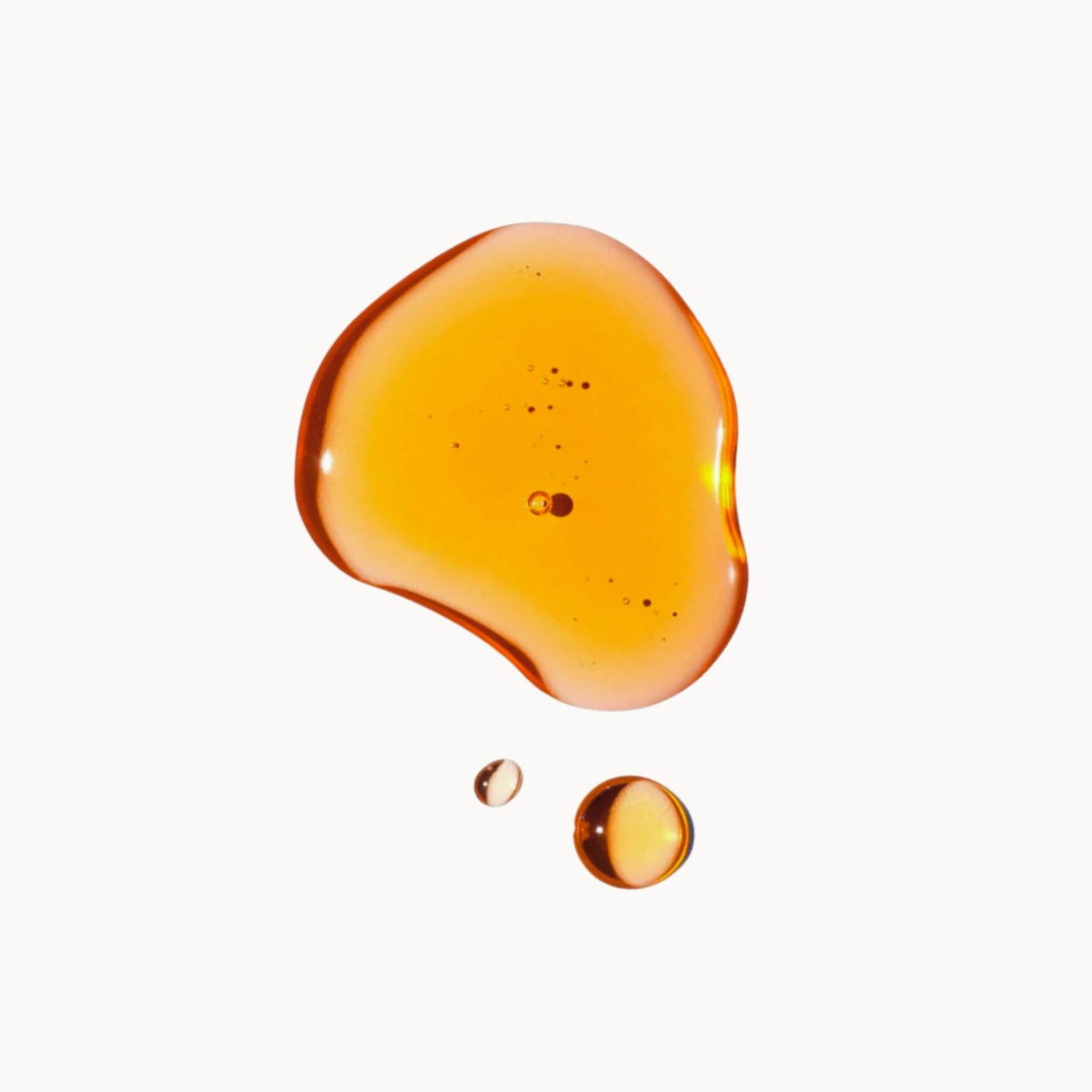 A large amber-colored rosehip oil drop with smaller droplets against a white background.